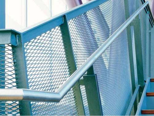Expanded metal stair railing with blue surface and diamond holes in public building.