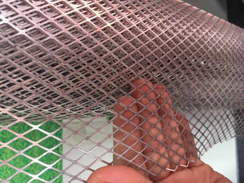  A roll of flattened expanded metal mesh with larger diamond holes, whose one side is touch by a hand.