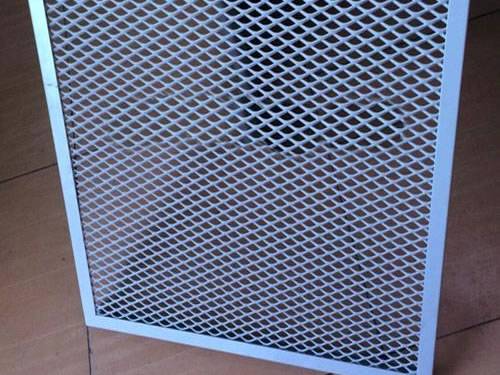 A blue expanded metal ceiling tile with diamond holes is standing on the floor, which is supported by one hand.