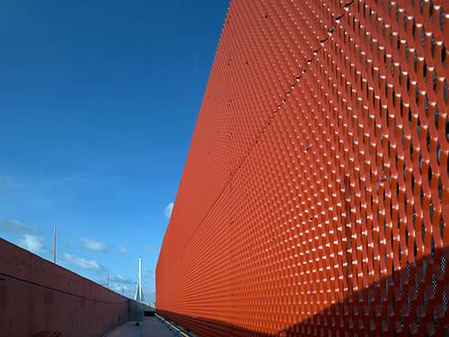 Architectural expanded metal with red surface and diamond holes is used as facade of large building.