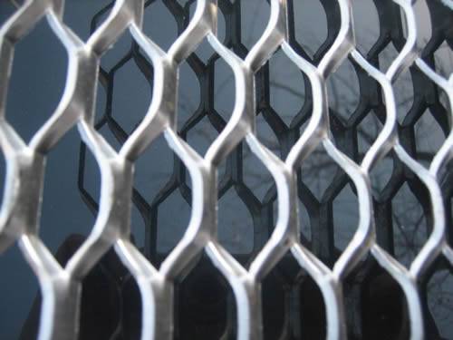 Raised heavy expanded metal fencing  with galvanized surface and hexagonal holes is in front of glass.