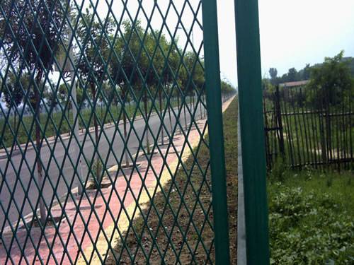 Expanded metal fencing with dark green surface and diamonds holes on the side of road.
